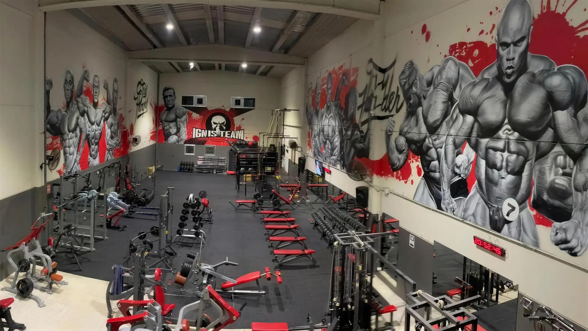 La sala de Ignis Gym: máquinas rojas y negras bajo murales de culturistas